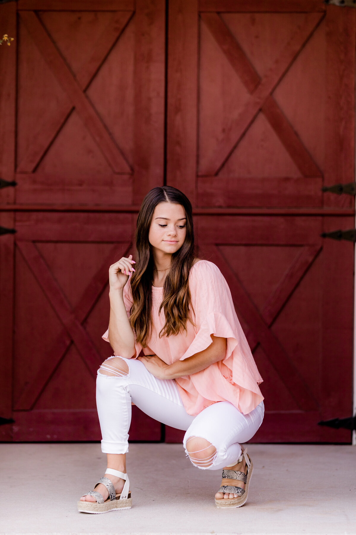 Brunette Senior girl does a crouch pose in front of a red barn door in downtown frankfort.