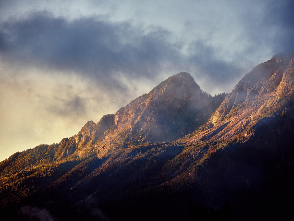 Herbstlich eingefärbte Berghänge des Dobratsch im Gegenlicht mit aufsteigendem Nebel – atmosphärische Landschaftsaufnahme mit warmem Lichtspiel