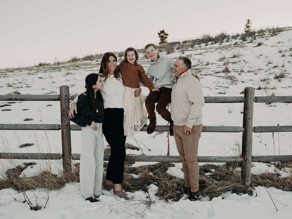 A family of five stylishly, dressed in winter cream, colored clothing poses organically along a fence on a Colorado farm just outside of Denver.