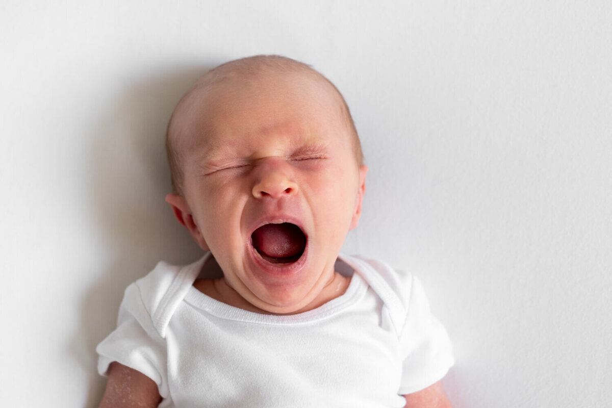 Ontspannen newborn shoot aan huis, met de baby op een zachte witte achtergrond.
