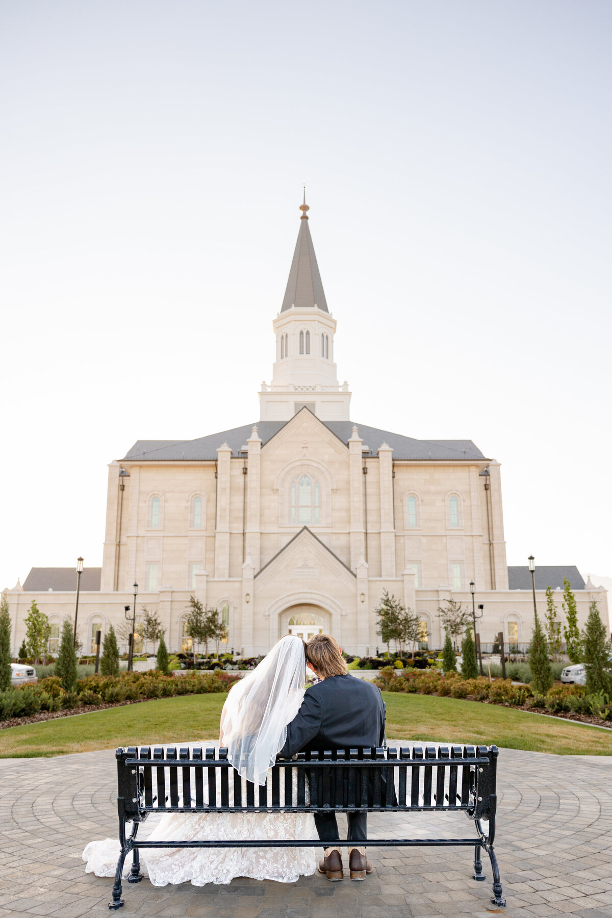 Newly married couple shares a quiet moment together sitting on a bench looking at the LDS temple.