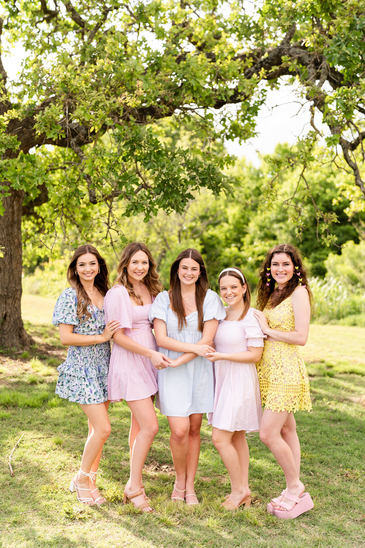 Texas A&M senior girls in pastel colors smiling and hugging each others elbows in the middle of nature at Leach Teaching Gardens