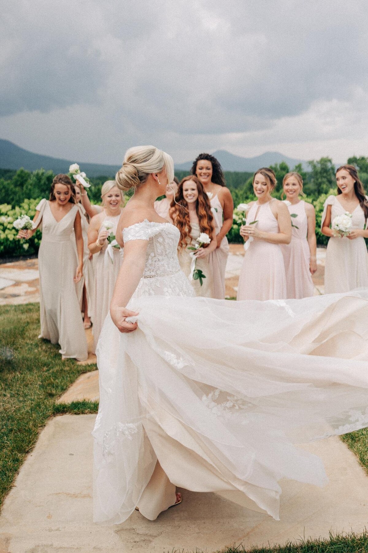 Bride in white dress with bridesmaids in pastel dresses, having a playful moment outdoors.