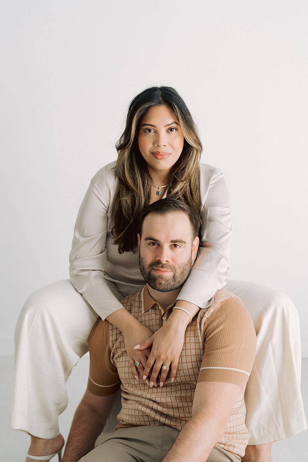 A man sits between his fiance's legs as they pose together for an engagement photo