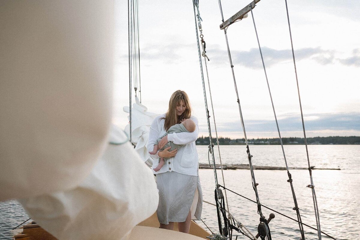 female holding newborn baby in blue blanket outdoors on sailboat