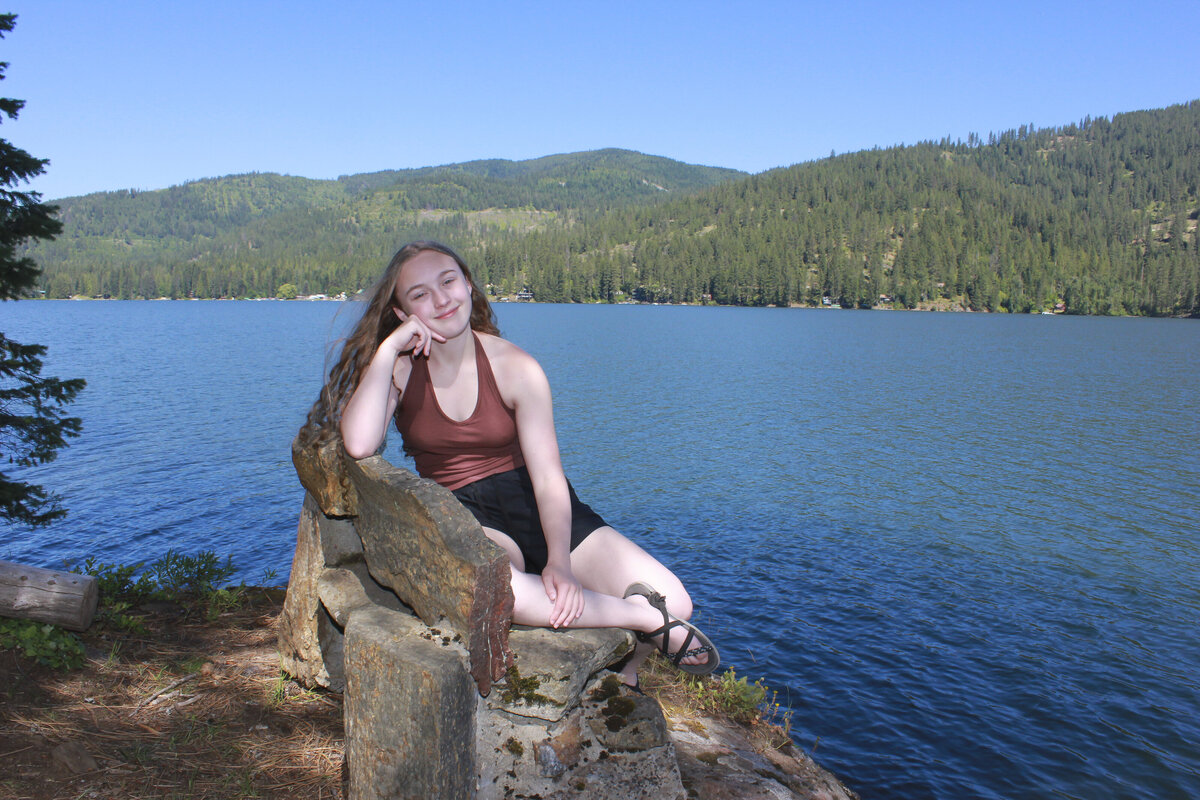 Graduating senior photo of young lady sitting on a bench on edge of Spirit lake smiling in the summer  breeze