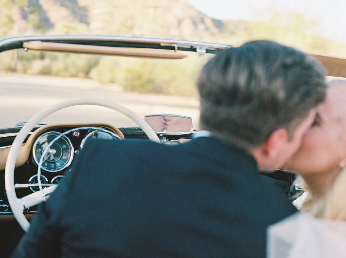 Romantic wedding photography capturing a just-married moment as the bride and groom share a kiss in their classic getaway car.
