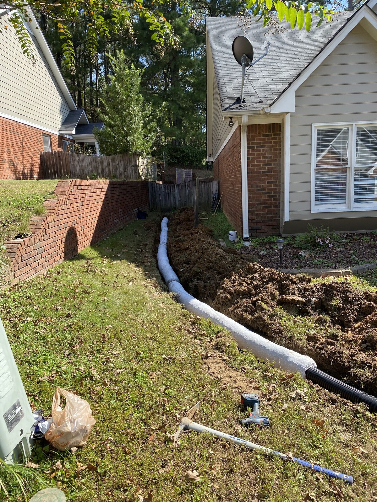 white-pipe-in-dirt-trench-between-house-and-brick-wall