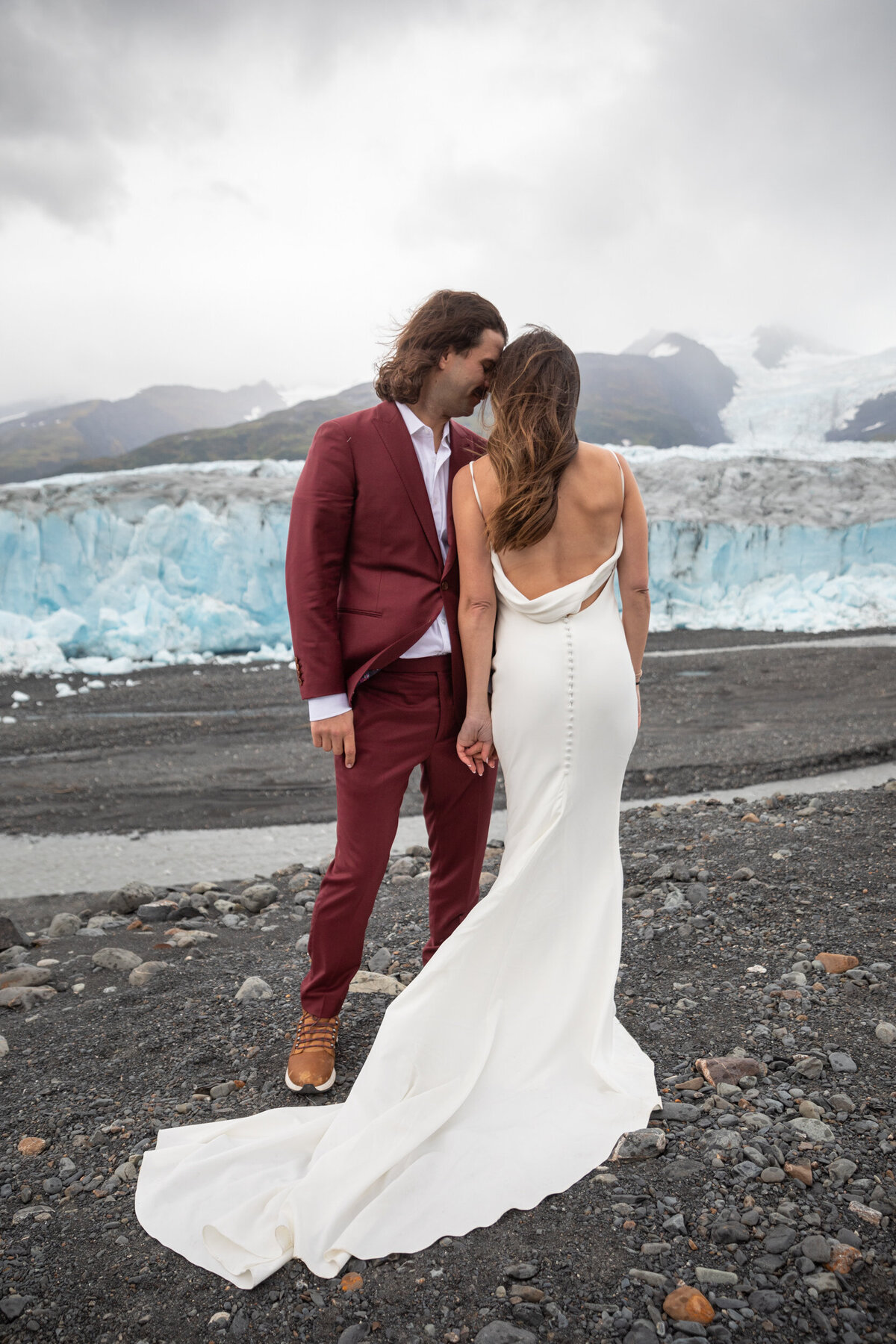 A bride and groom stand shoulder to shoulder in front of a glacier in Alaska.