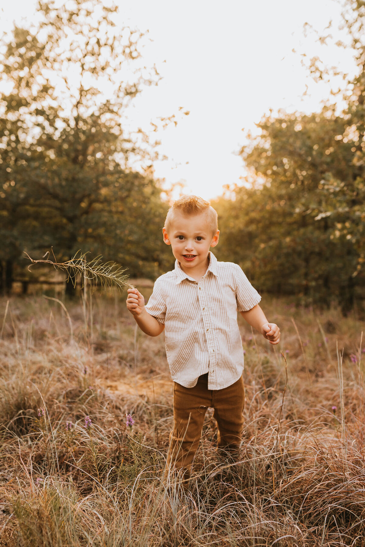 Blonde toddler boy playing with a stick in a field