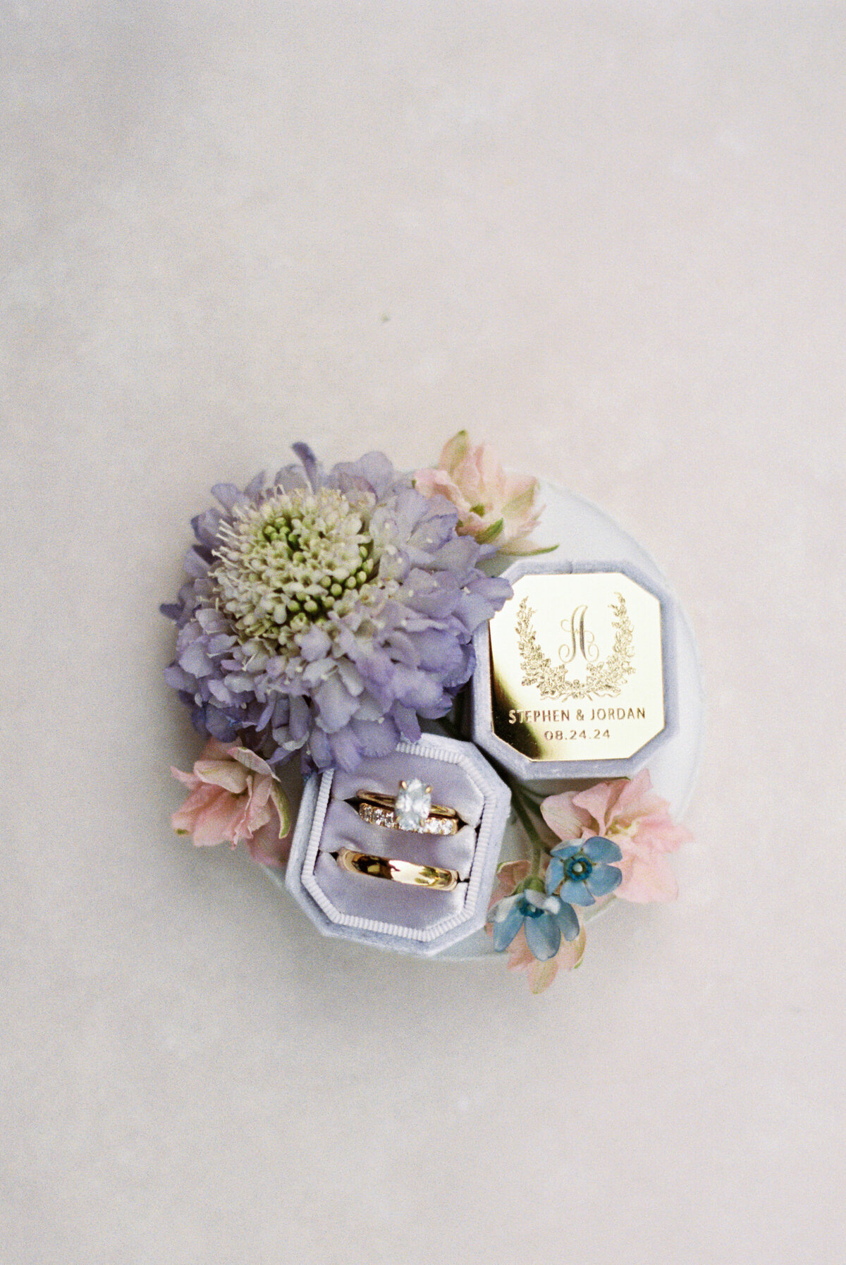 Close-up of wedding rings with custom crest ring box and fresh flowers at Gervasi Vineyard wedding.