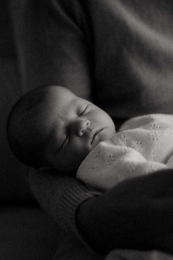 Bébé dort paisiblement dans les bras d’un parent. Séance photo naissance à domicile par Kamescop, photographe en Loire-Atlantique