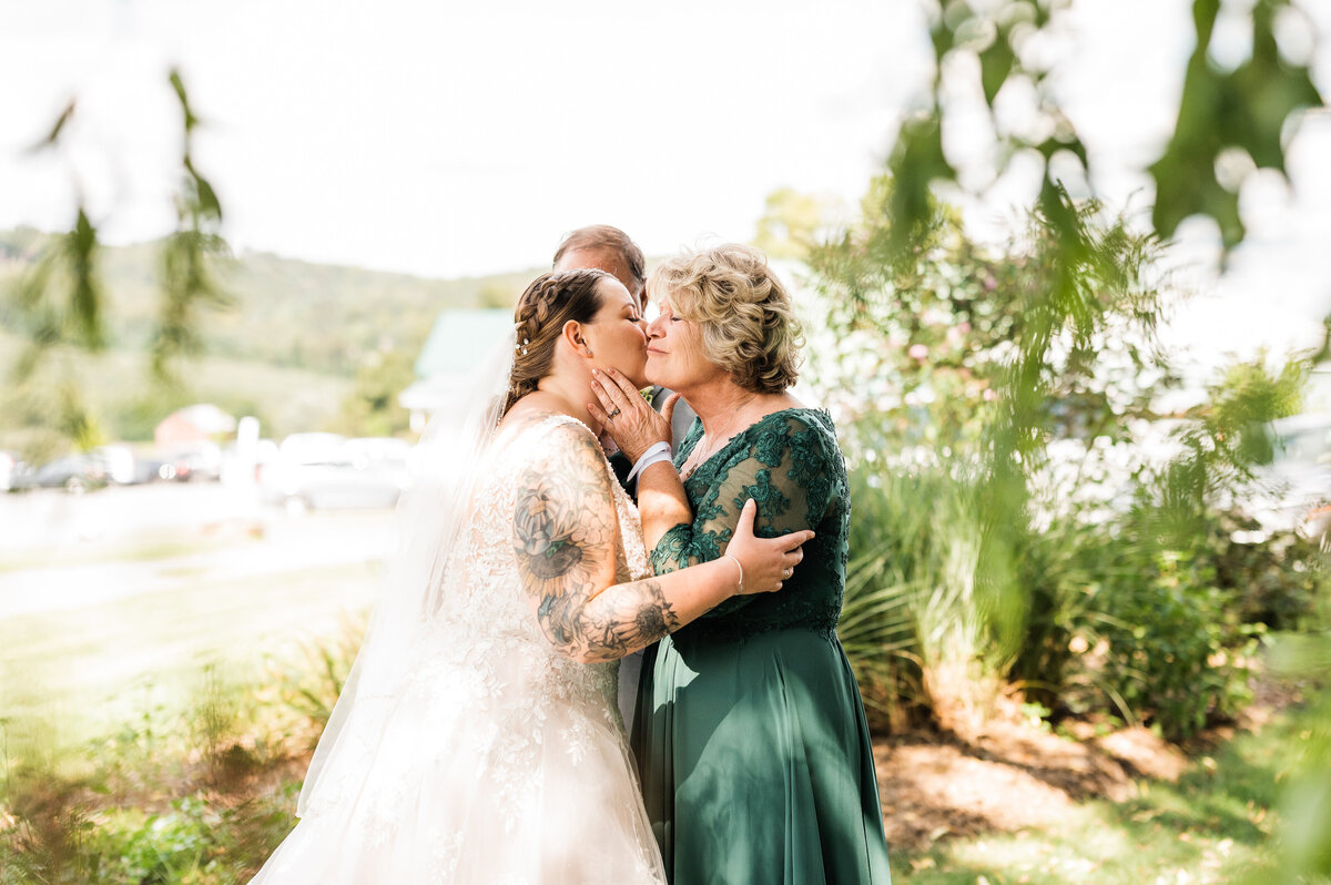 mother of the bride meets her under a willow tree and kisses her cheek with a mountain range in the distance for a Shenandoah wedding