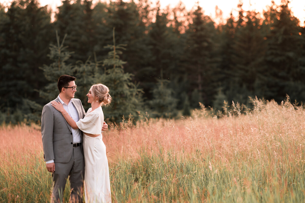newly engaged couple standing in a field smiling at each other