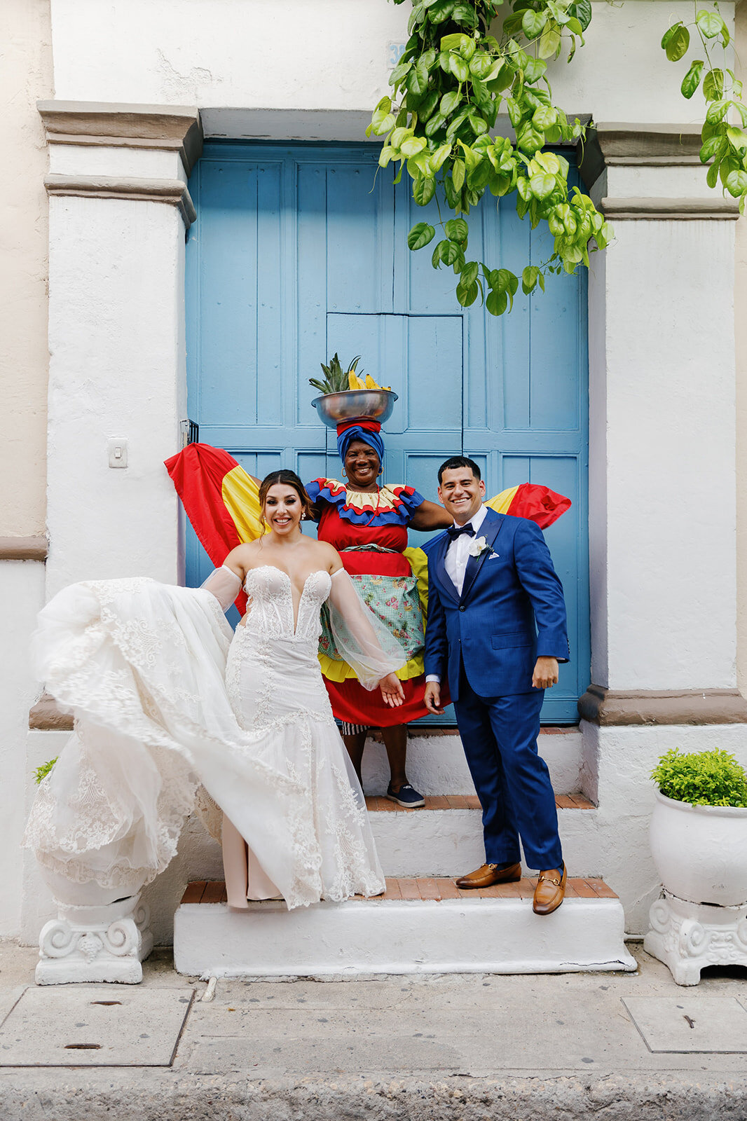 Victoria lifts her wedding dress playfully while posing with Daniel and a local Palenquera, adding a fun cultural touch to their Cartagena wedding portraits.