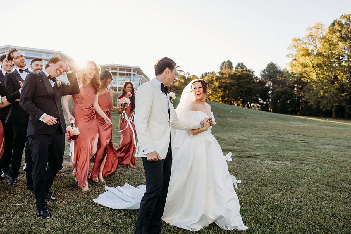 Bride and groom walking and laughing with bridesmaids walking behind them