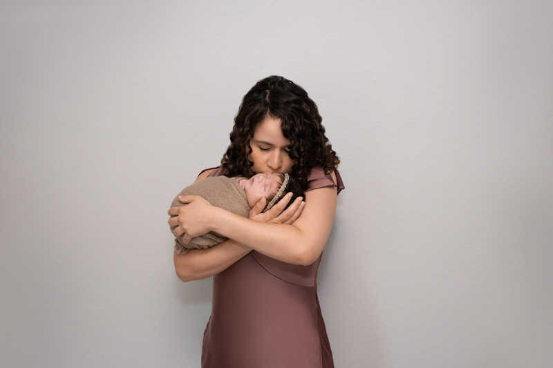 Mother in blush dress holding baby during Houston newborn family photoshoot.