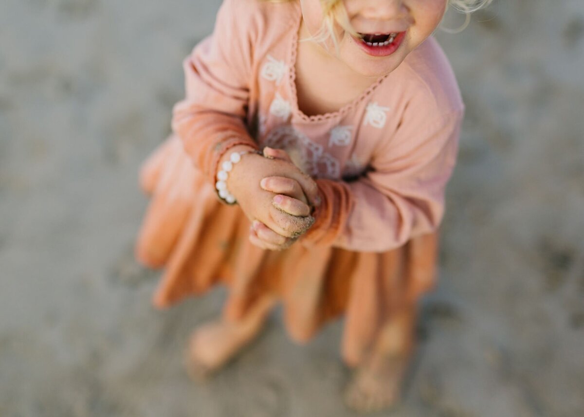 A little girl, smiling with her sandy hands.