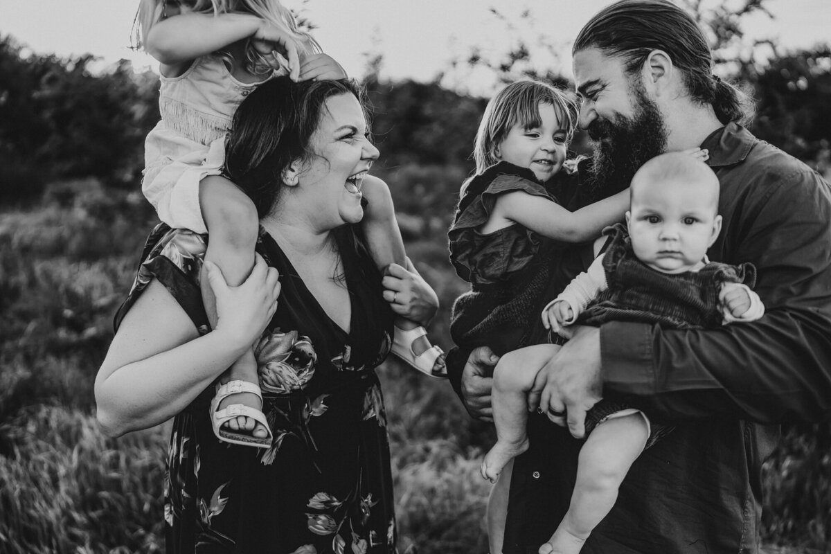 Black and white family photo of parents laughing while carrying their two young children, San Diego family photography.