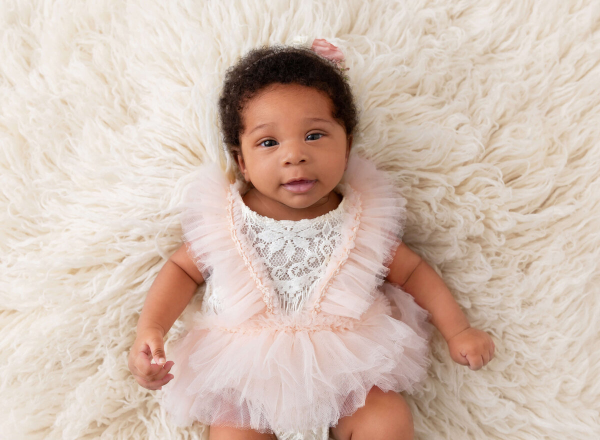 Aerial shot of a baby girl in a blush romper holding a wooden toy, taken during a NYC baby milestone photoshoot