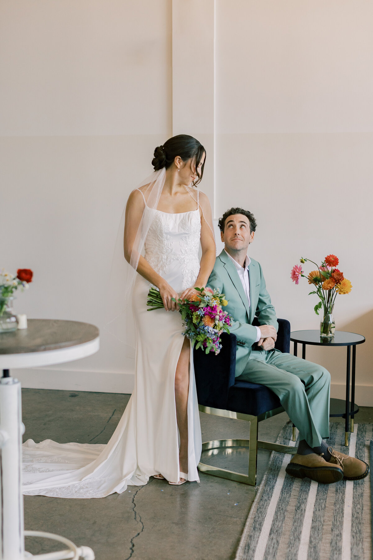 Sara holding vibrant bouquet by Crimson & Clover standing beside Brendan in modern indoor portrait at Fetewell wedding.