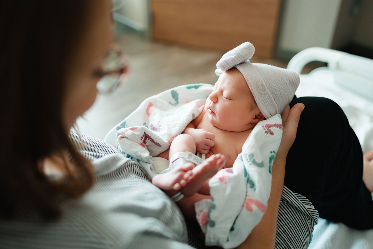 An expert in maternity photography captures a beautiful hospital moment of a mom with her newborn daughter, wrapped snugly in a blanket. The tender scene showcases the intimate and emotional first moments between mother and child.