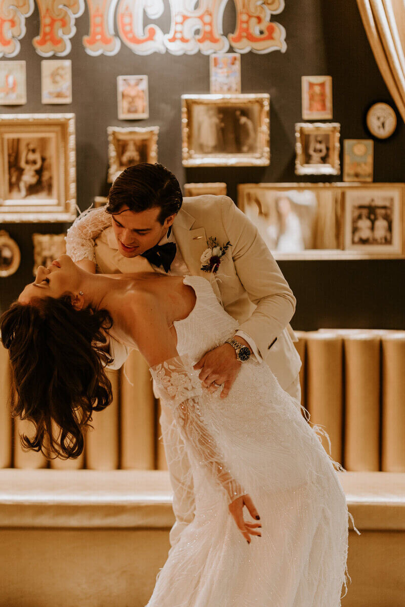 Marié basculant la mariée en arrière et s'apprêtant à lui faire un bisou dans le cou dans un décor vintage pour la séance photo mariage.