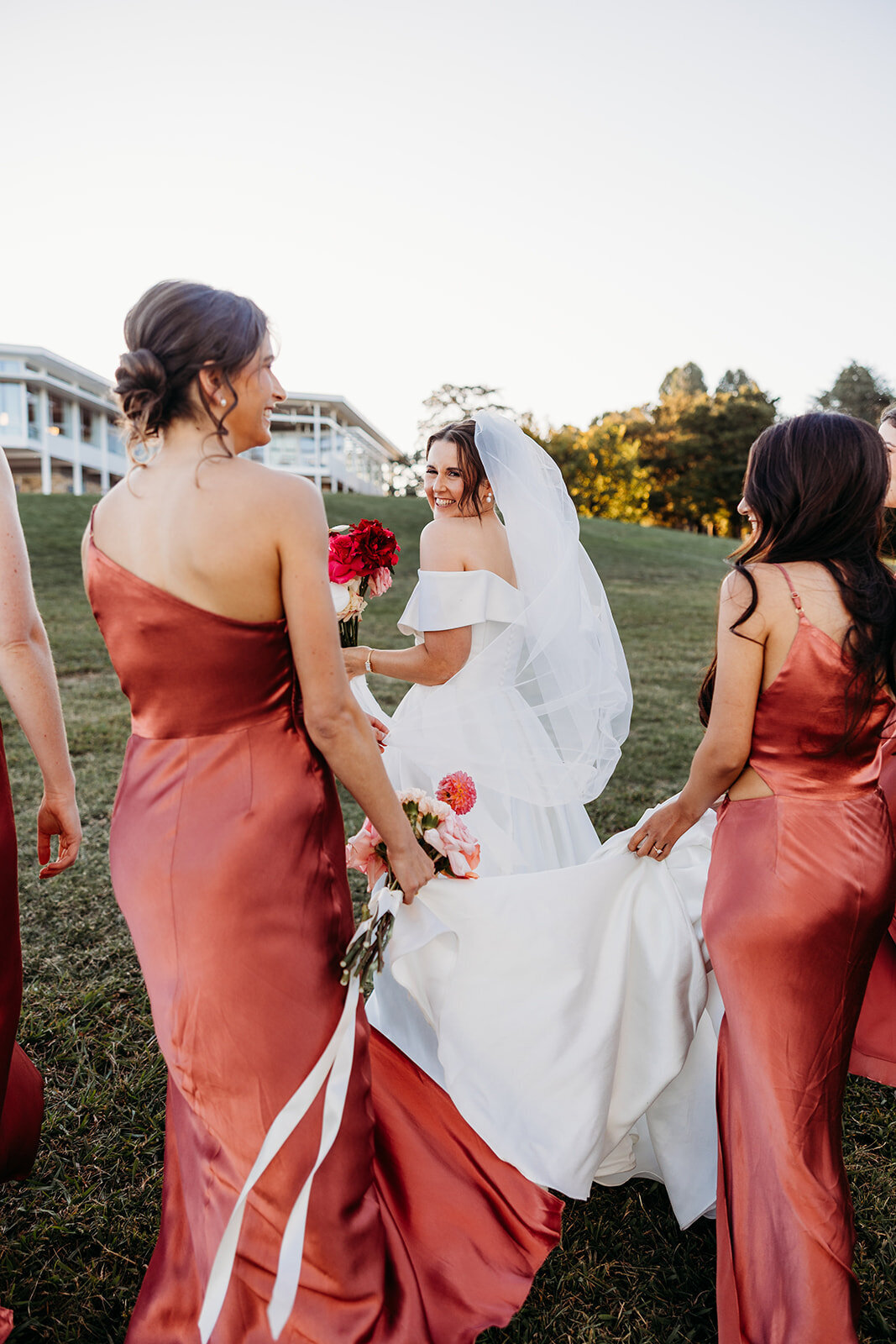 Bride overlooking her shoulder while her bridesmaids carry the train of her wedding dress. The Marion wedding venue shown in the background