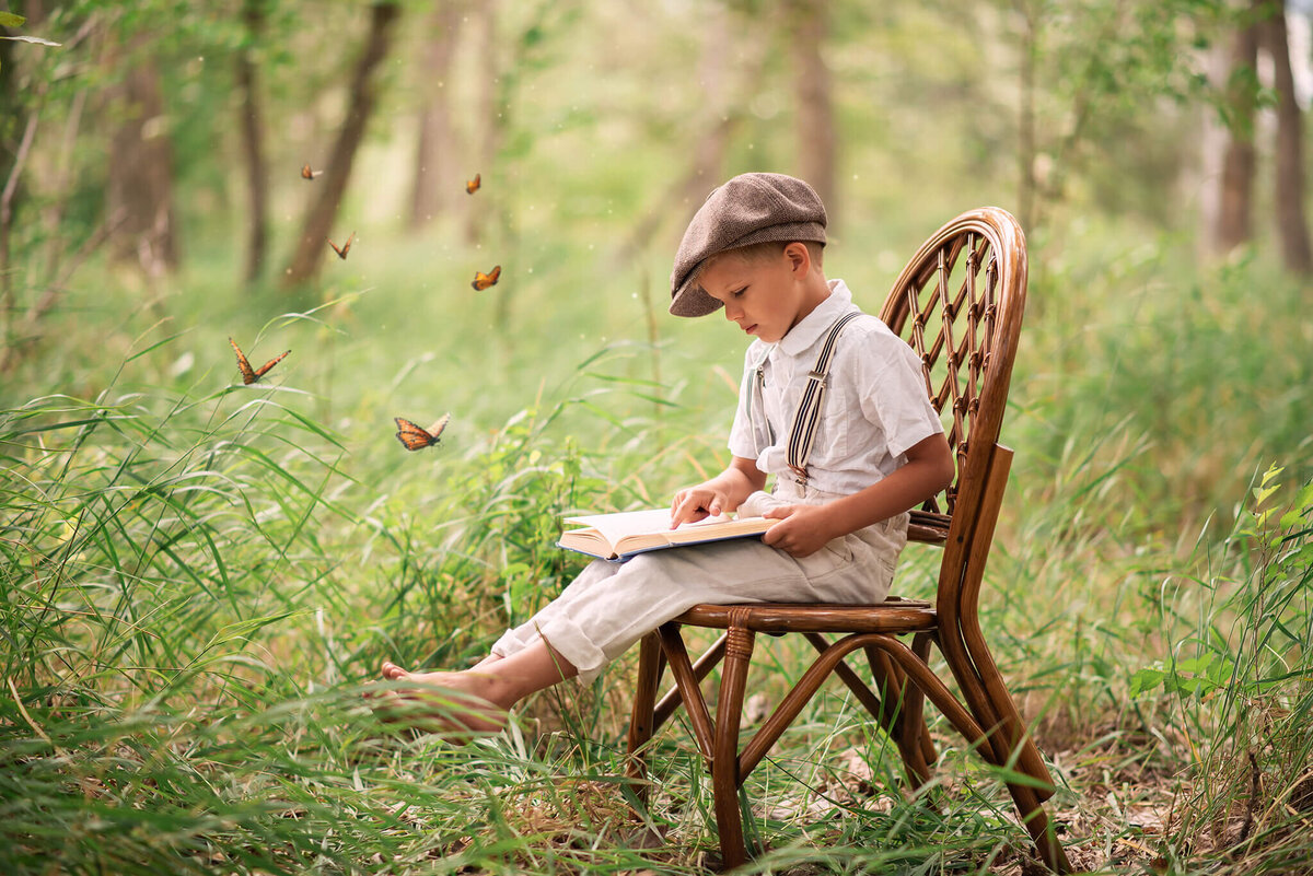 Little boy sitting on a wooden chair in the grass reading a book. Brittany Danielle captures this portrait in Kamloops.