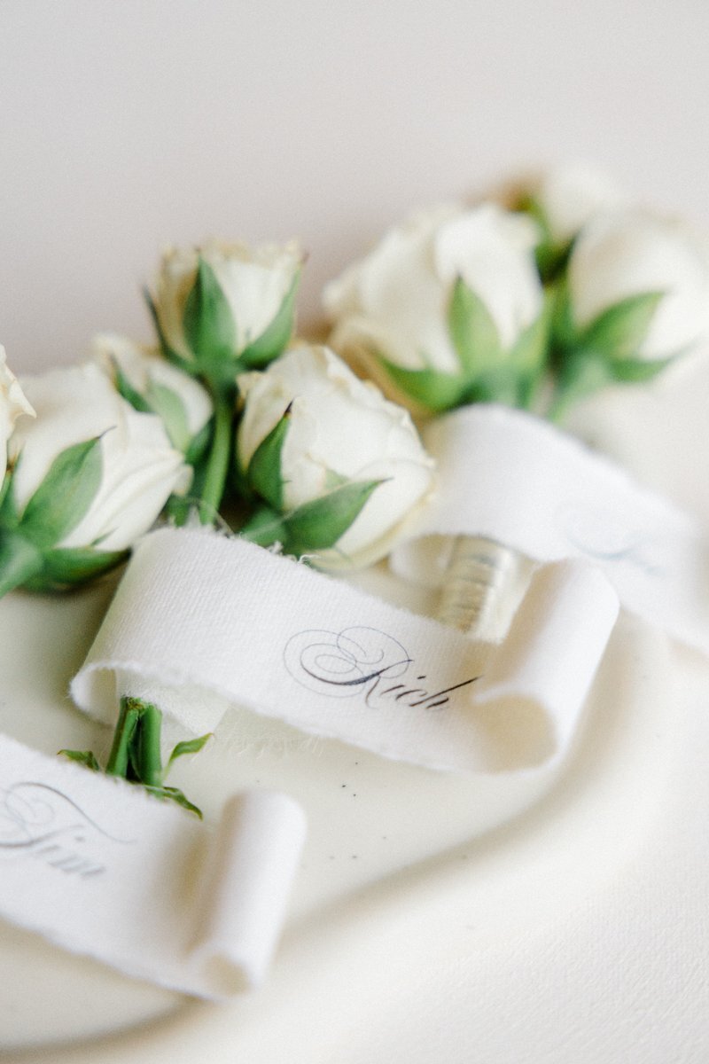 Detail of a wedding boutonnieres on a white dish together with name tags on the side