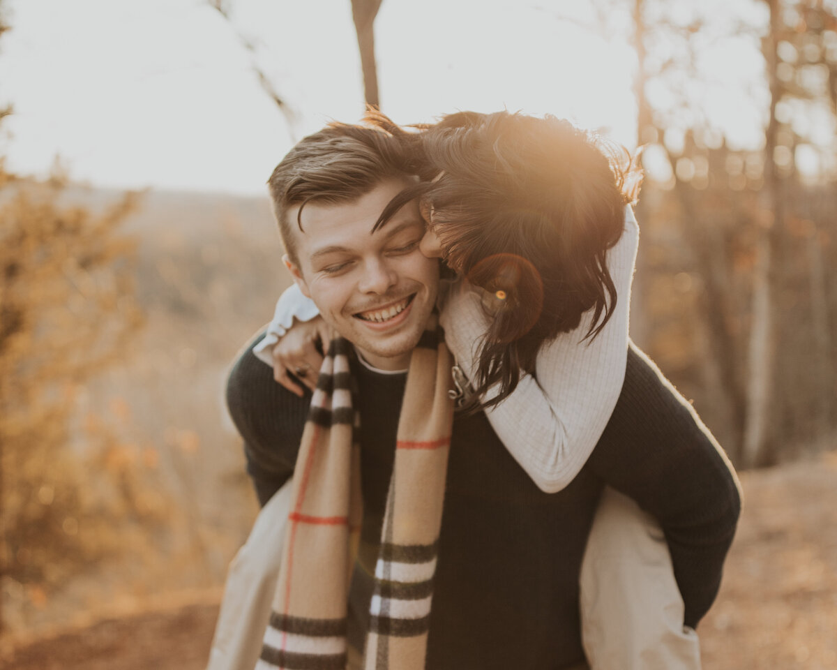 piggy back ride girl kissing boy with sun during fall