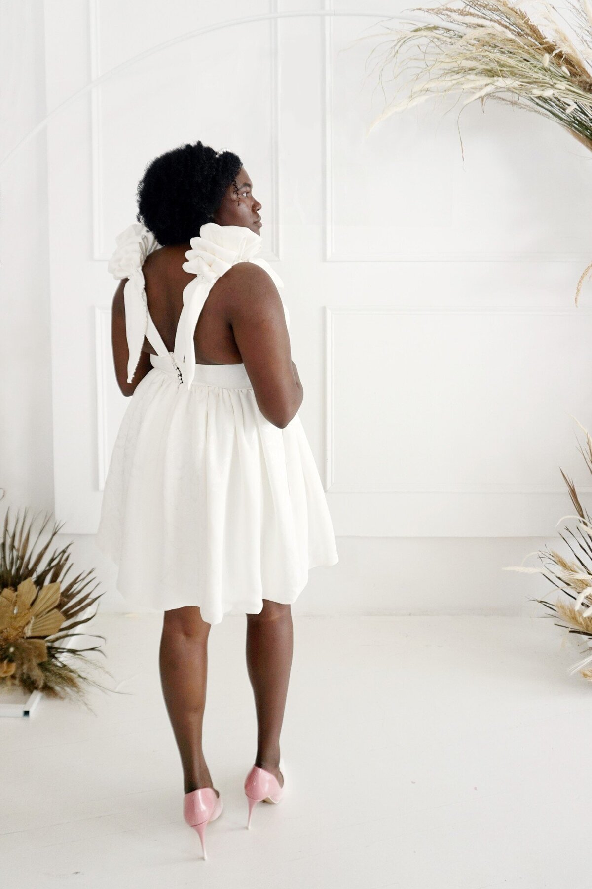 Side back view of the short Taylor wedding dress style, which features a v-back and statement shoulder ruffle details.