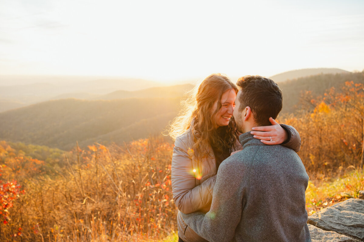 A couple leans in for a kiss surrounded by fall colors.