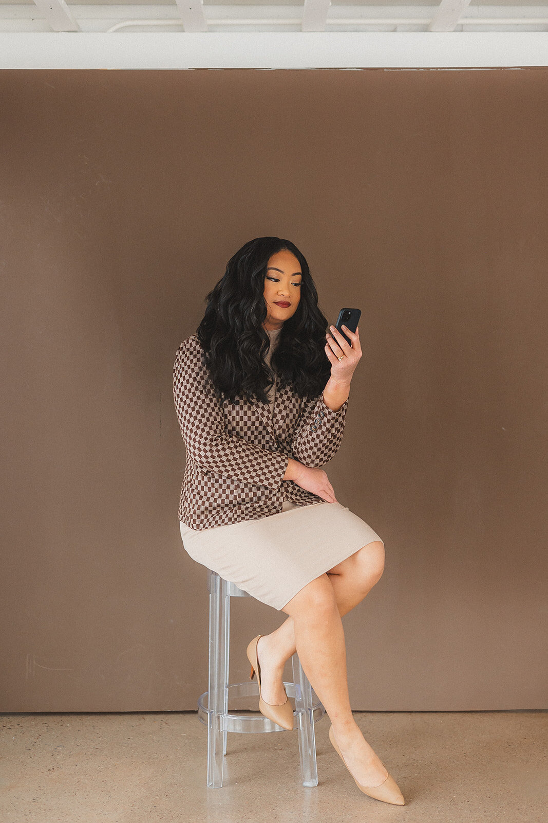 A woman seated on a stool, intently gazing at her phone