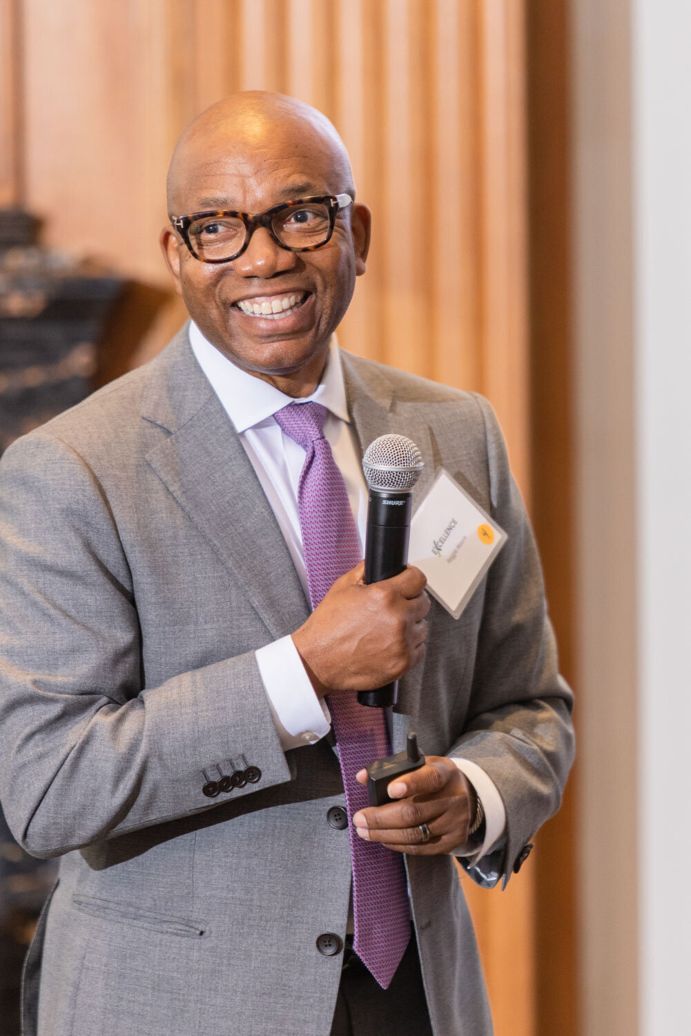 Smiling man in gray suit holding microphone during event