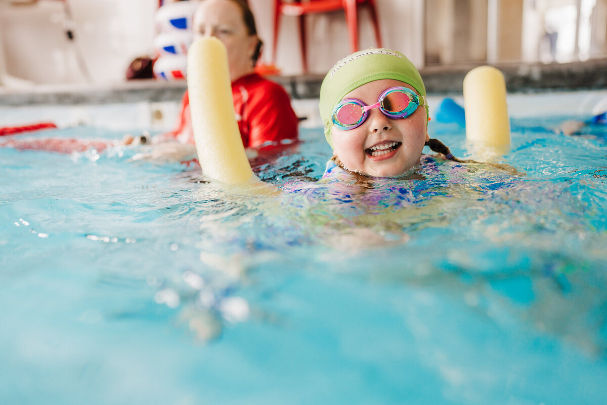 girl with goggles smiles on a pool noodle