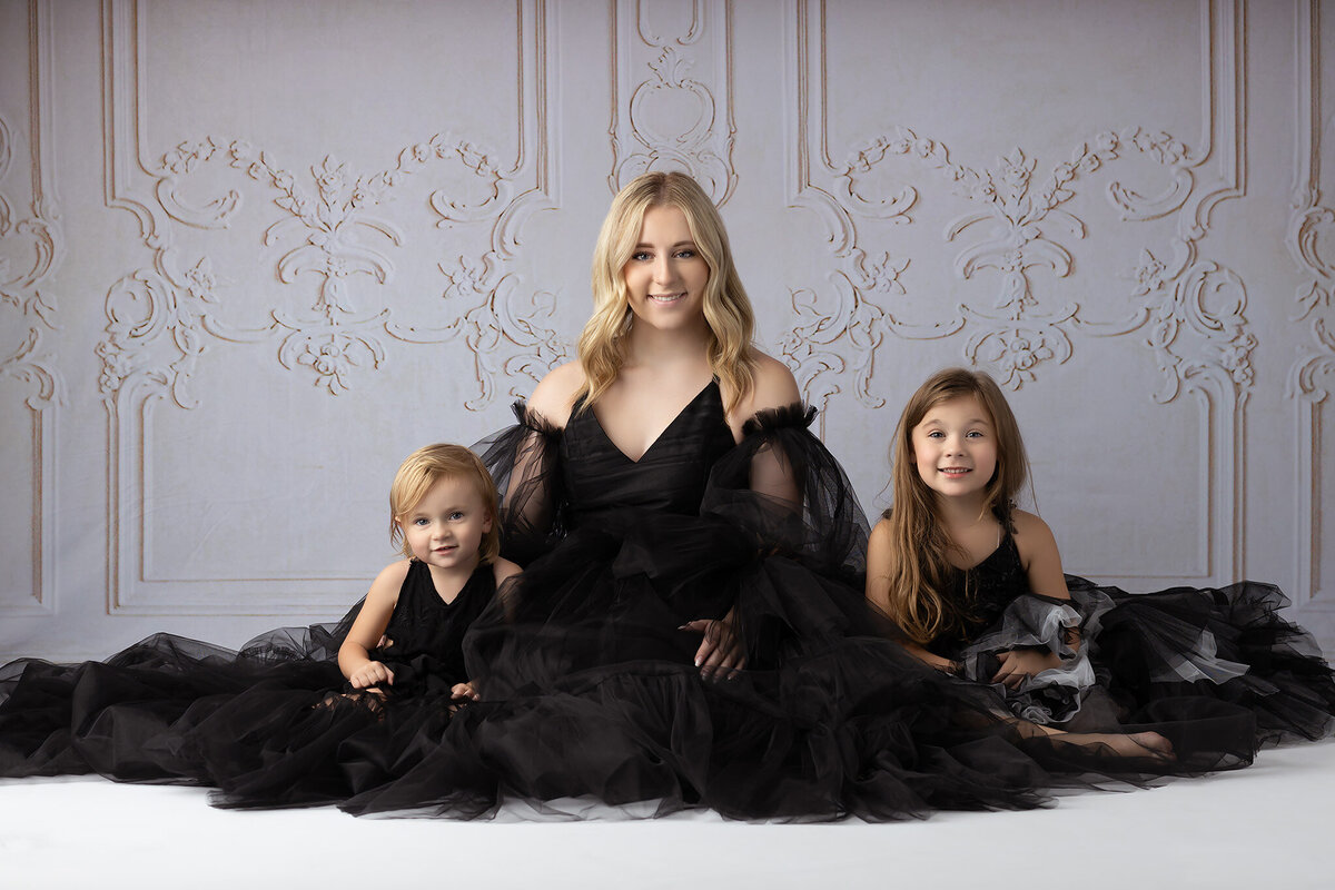 A family portrait featuring a sisters dressed in black tulle dresses, posed on a white background. Dallas family photographer.