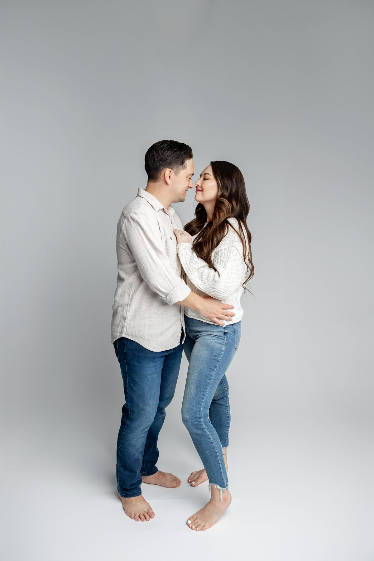 Couple standing closely together, smiling while holding hands in studio setting. Photographed by Yucaipa family photographer Kaitlyn Dawn Photography.