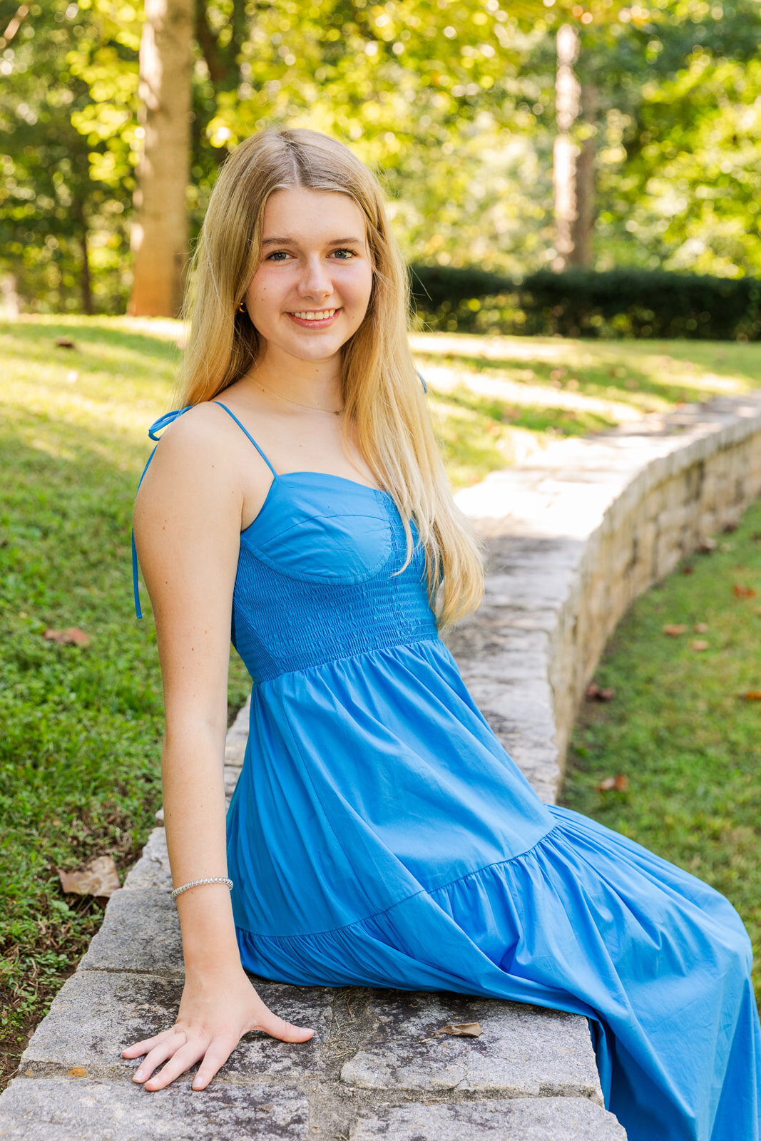 High school senior girl wearing a blue dress and sitting on a park wall during photo session in Atlanta with Laure Photography