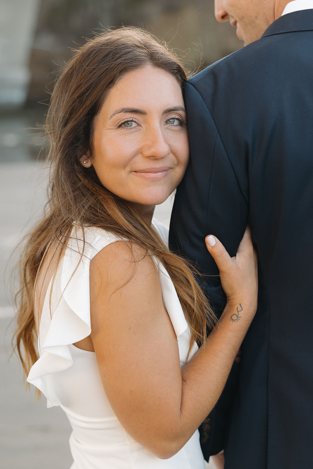 Bride to be smiling over her fiance's shoulder on the beach