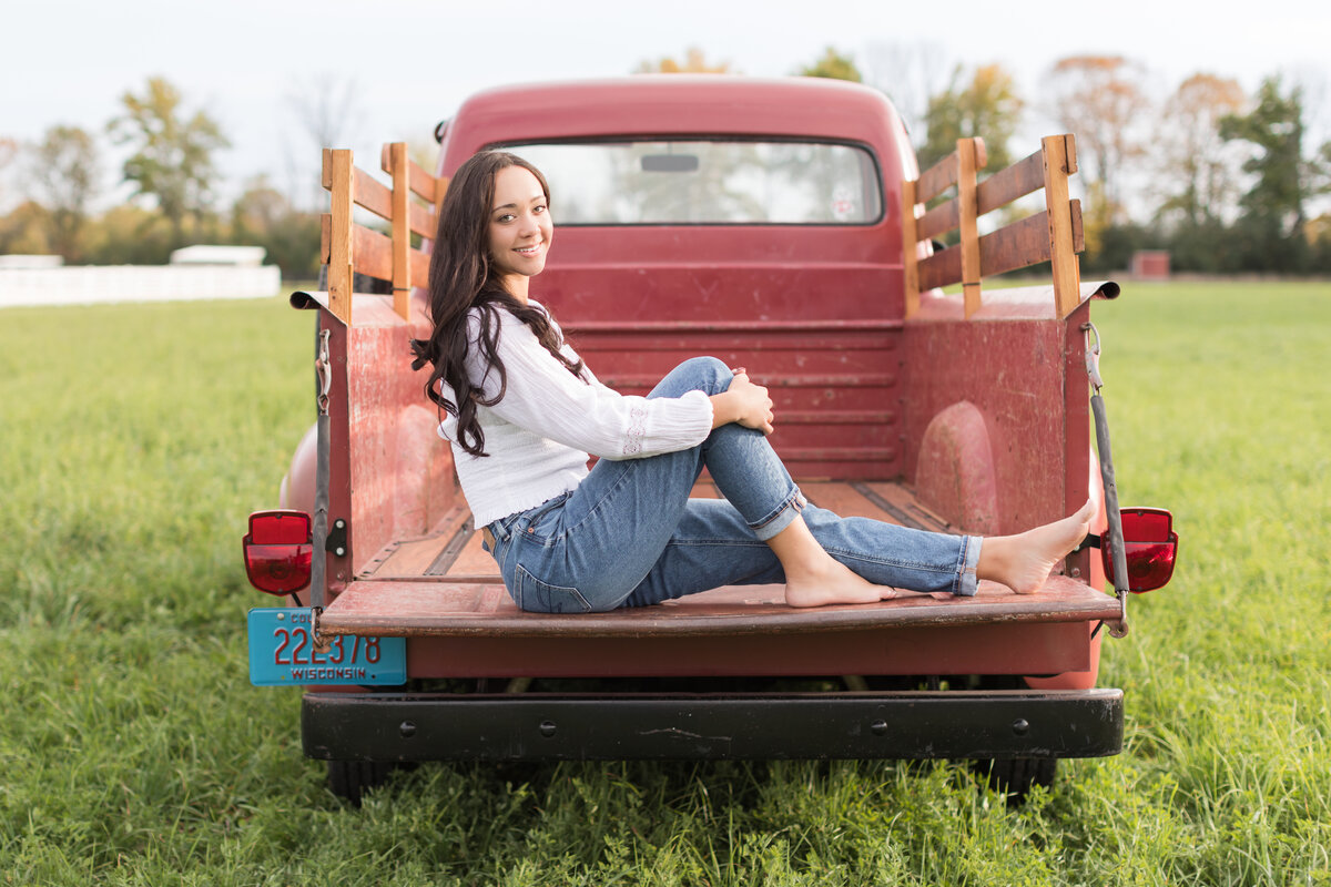 Senior girl seated in the back of an old red truck smiling at the camera