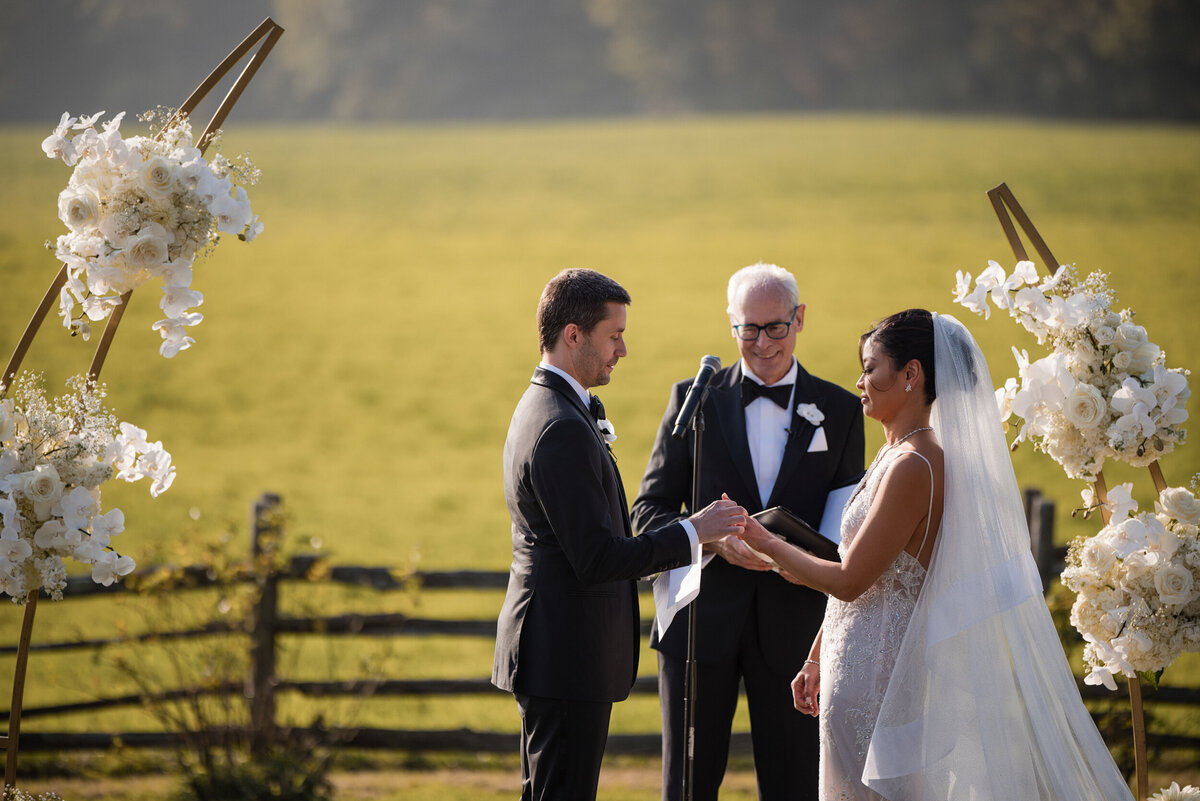 A couple gets married outside surrounded by white arched flowers at a destination wedding in Vermont