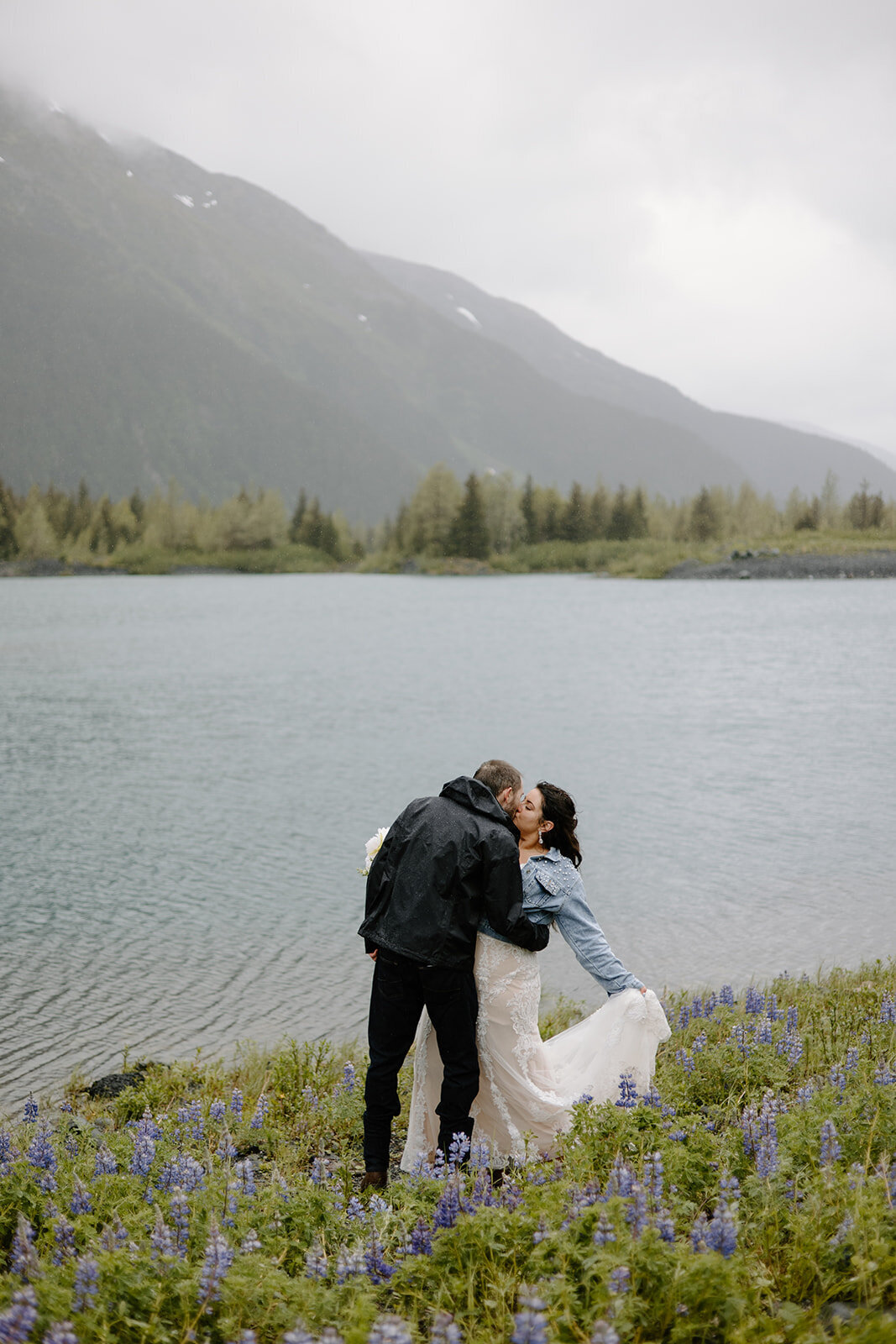 Elopement couple shares dip kiss by misty Alaska lake and mountain.