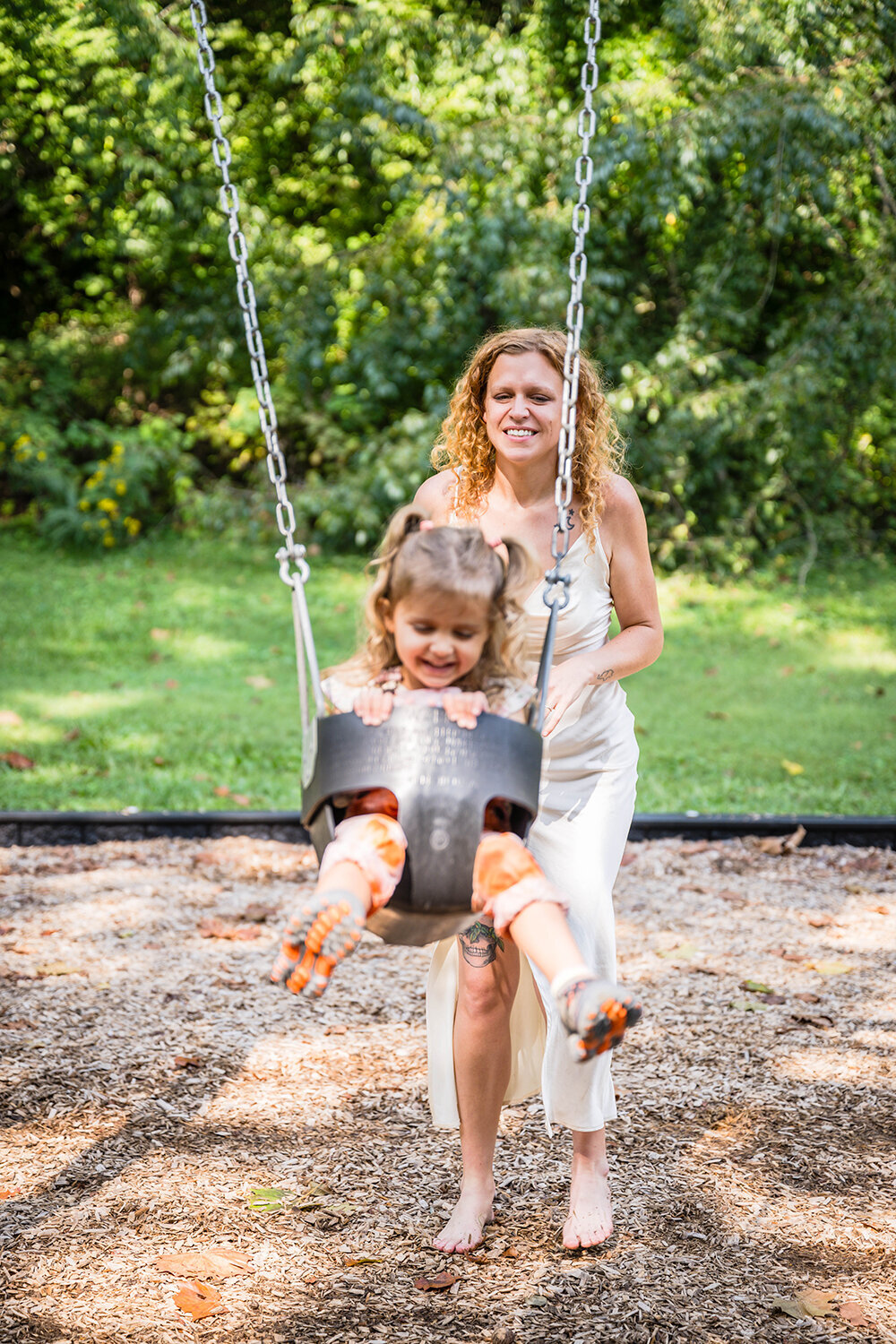 A parent pushes her child in a swing at the playground at Fishburn Park and smiles as her toddler giggles.