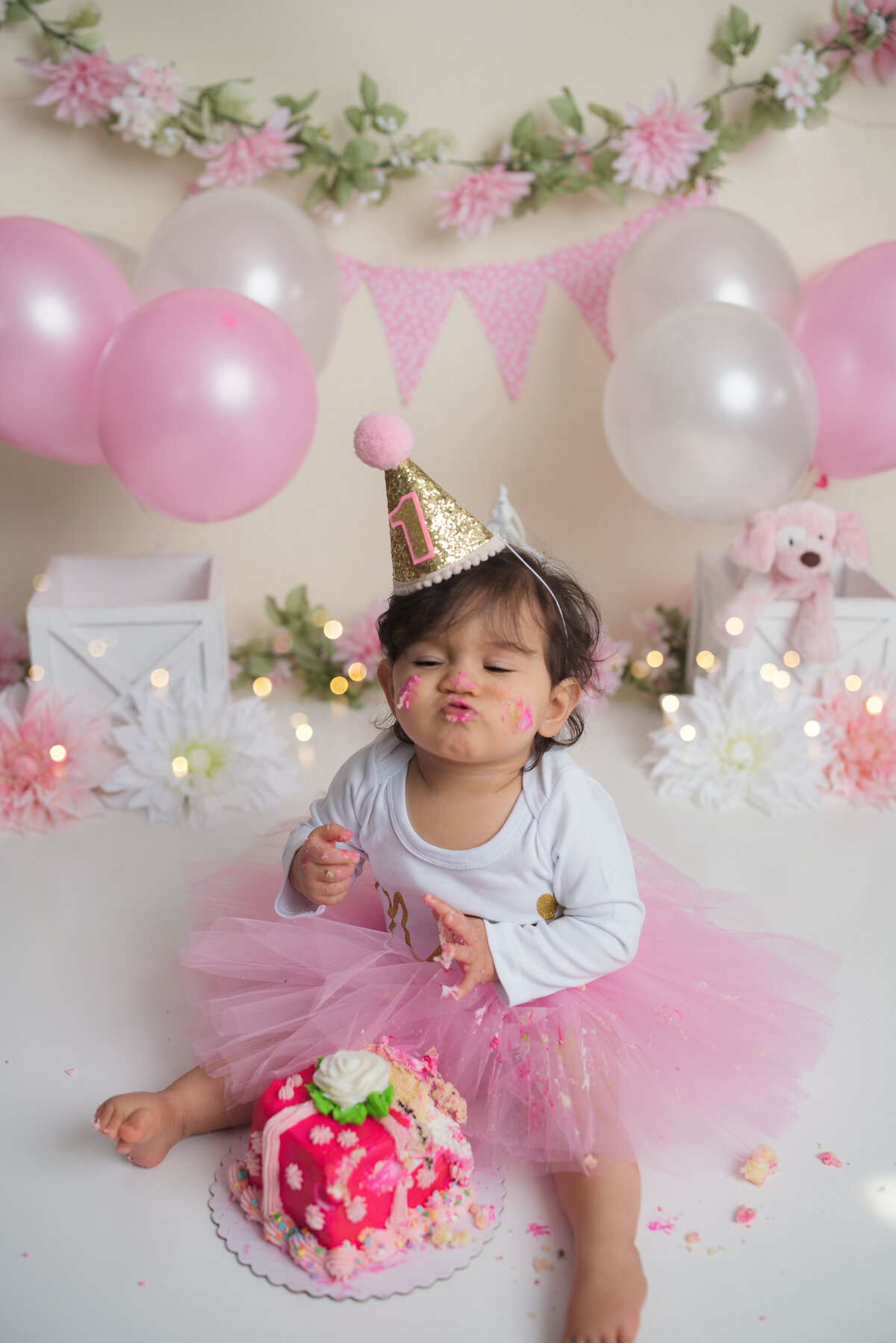 One year girl eating a pink cake wearing pink tutu with white shirt and part hat on head