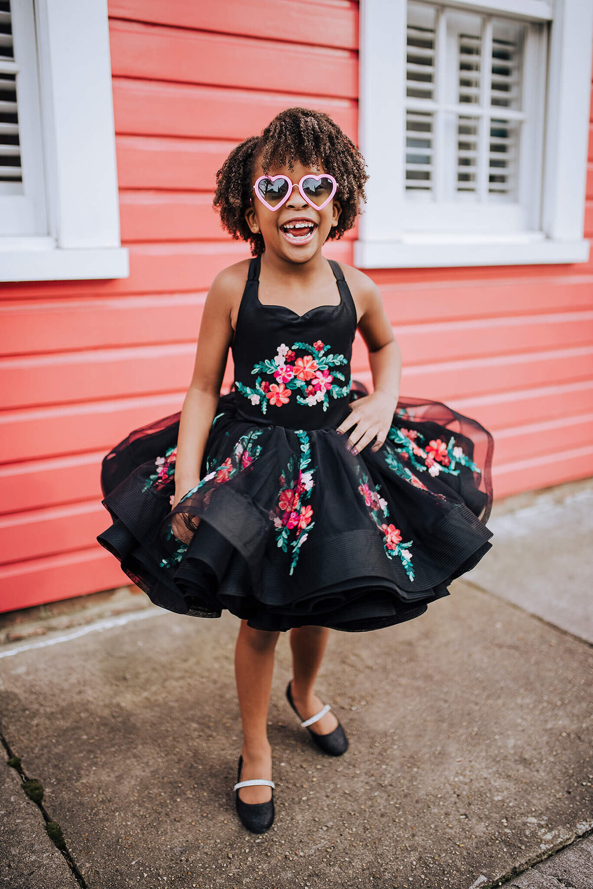African American girl with pink hearts glasses and black shoes in a black dress with pink flowers laughing in Fells Point Baltimore Maryland