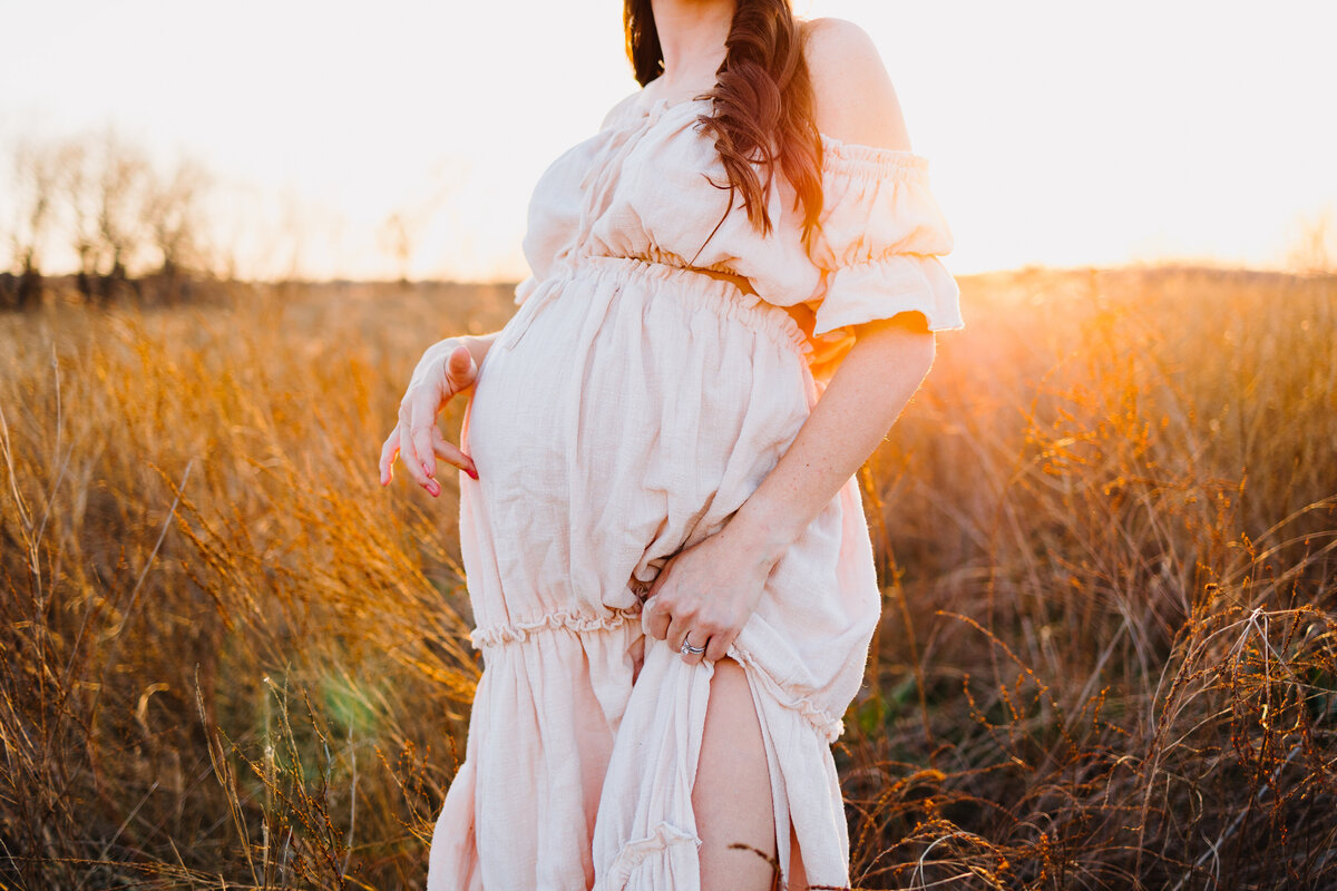Photo of the belly of a pregnant woman in a garden, she is wearing a long white dress