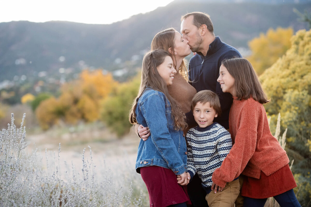 Three siblings hug and play whiel mom and dad hug behind them