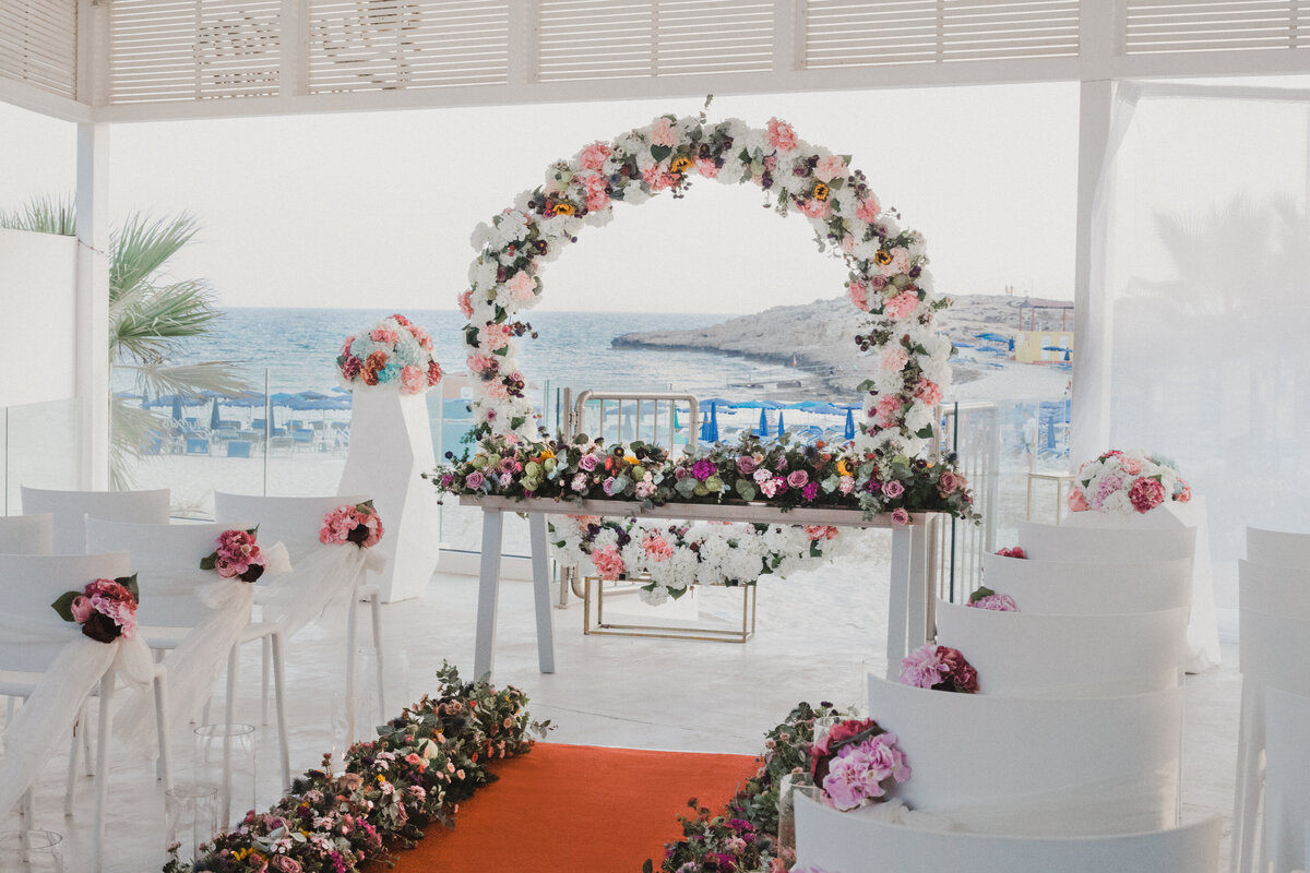 A round floral arch set infront of a seaview with an aisle lined with flowers