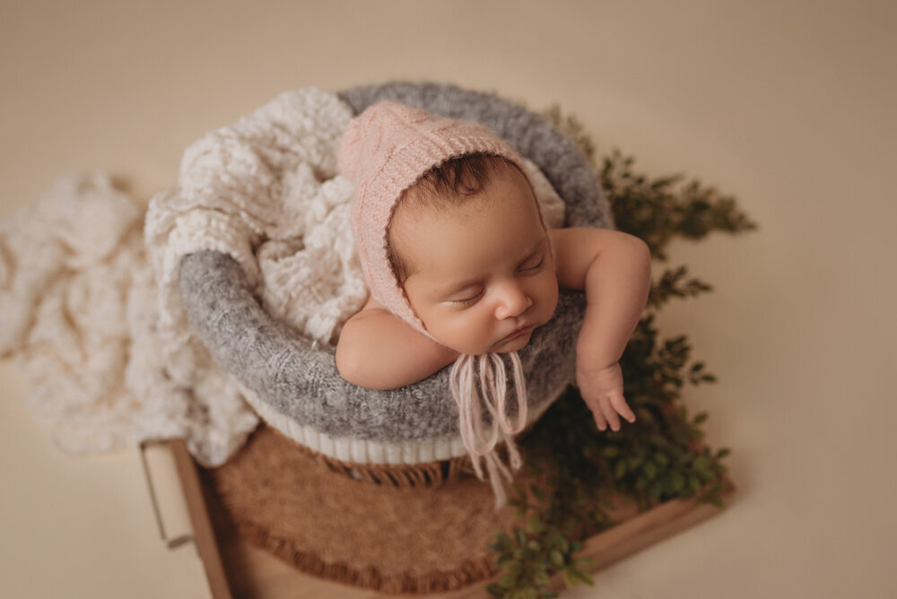 Newborn photo shoot photographed by Atlanta, Georgia newborn photographer with baby posing on neutral fabric with dainty headband on and sleeping posed in a basket.
